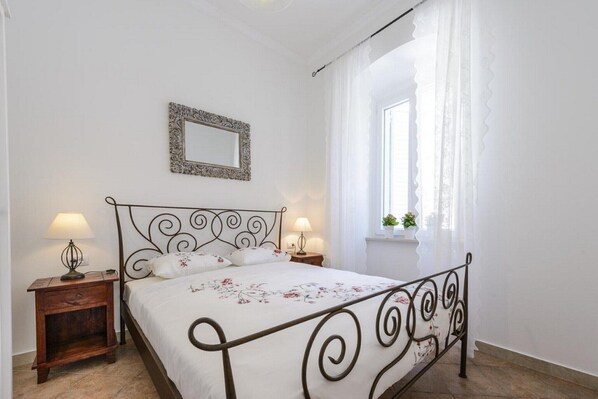 Un dormitorio con una cama, dos mesitas de noche con lámparas, un espejo en la pared y una ventana con cortinas.