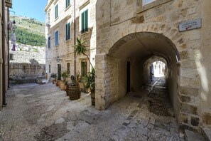 Una estrecha calle de piedra con un pasaje en arco, plantas en macetas y un cartel que indica zona peatonal.