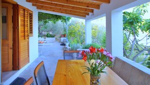 Un patio al aire libre con una mesa y sillas de madera, techo de madera y vista a la vegetación.