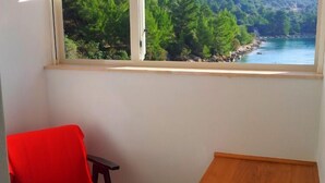 Habitación con ventana que da a una zona boscosa y un cuerpo de agua. Hay una silla roja y una pequeña mesa de madera.