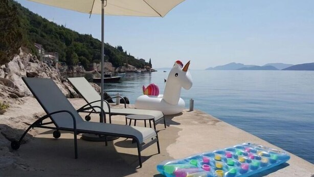 Un área de descanso en la playa con sillas reclinables, un unicornio hinchable blanco y una bolsa de hielo colorida sobre la arena.