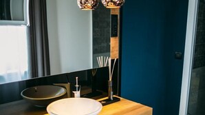 Een moderne badkamer met een houten wastafelmeubel, een witte wasbak, een spiegel en een hoge, decoratieve vloerlamp.