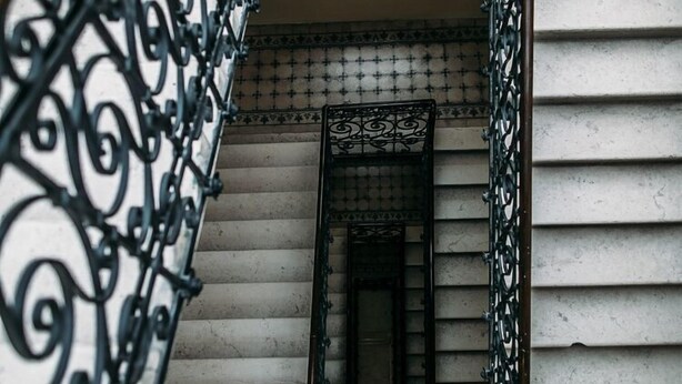 Escadaria com grades de metal preto ricamente decoradas e parede revestida com azulejos estampados.