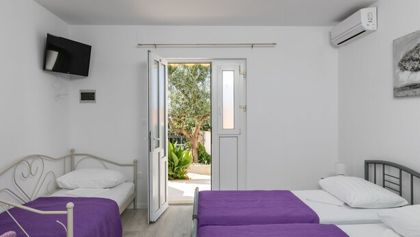 Una habitació amb dos llits, un televisor muntat a la paret i un aparell d'aire condicionat.
