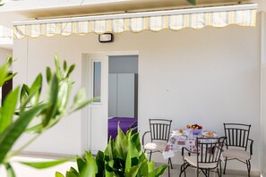 Un petit espace extérieur aménagé pour prendre les repas, avec une table pour deux personnes, une chaise et une porte donnant sur une pièce.