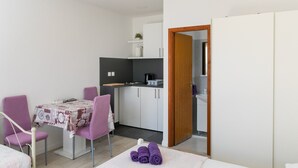 Una habitación compacta con una mesa de comedor, sillas moradas, una pequeña cocina y un armario.