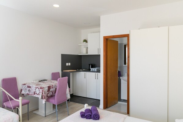 Una habitación compacta con una mesa de comedor, sillas moradas, una pequeña cocina y un armario.