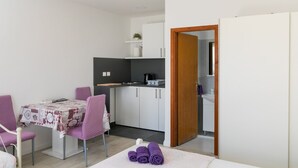 Habitación compacta con una mesa de comedor, sillas moradas, una pequeña cocina y una puerta de madera.