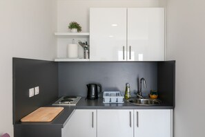A modern kitchen with a black countertop, white cabinets, a kettle, a sink, and a cutting board. - Apartments Karol&Mara-Studio Aparment 1 (Mlini)