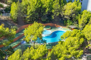 Une vue aérienne d’une piscine entourée d’arbres, avec un petit pavillon et un espace de repos couvert.