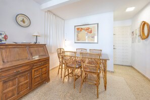 Uma sala de jantar com um armário de madeira, cadeiras de vime, uma mesa e um quadro na parede.