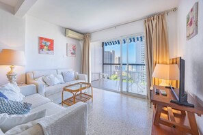A modern hotel room with a balcony, a sofa, a TV, and a lamp.