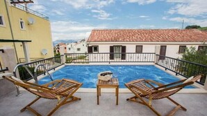 Ein Swimmingpool mit zwei Holzliegen und einem Tisch, umgeben von einem Metallgeländer.