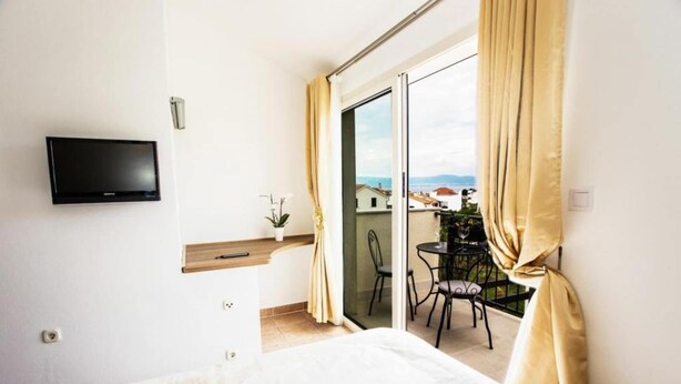 Ein Hotelzimmer mit einem Bett, einem an der Wand befestigten Fernseher, einem kleinen Tisch mit einer Pflanze und einem Balkon mit Tisch und Stühlen.
