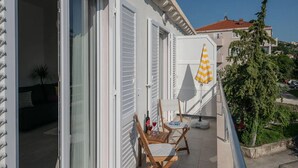 Ein Balkon mit weißen Fensterläden, einem gelb-weiß gestreiften Sonnenschirm und einem Tisch mit Stühlen.