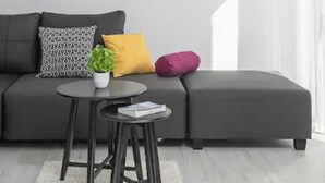 Ein modernes Wohnzimmer mit einem grauen Ecksofa, einem kleinen runden Tisch und einer Topfpflanze.