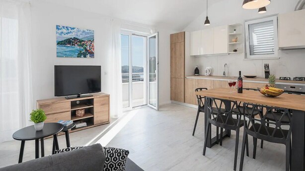 Eine moderne Wohnung mit Wohnzimmer, Essbereich, Küche und einem Balkon mit Blick auf die Stadt.