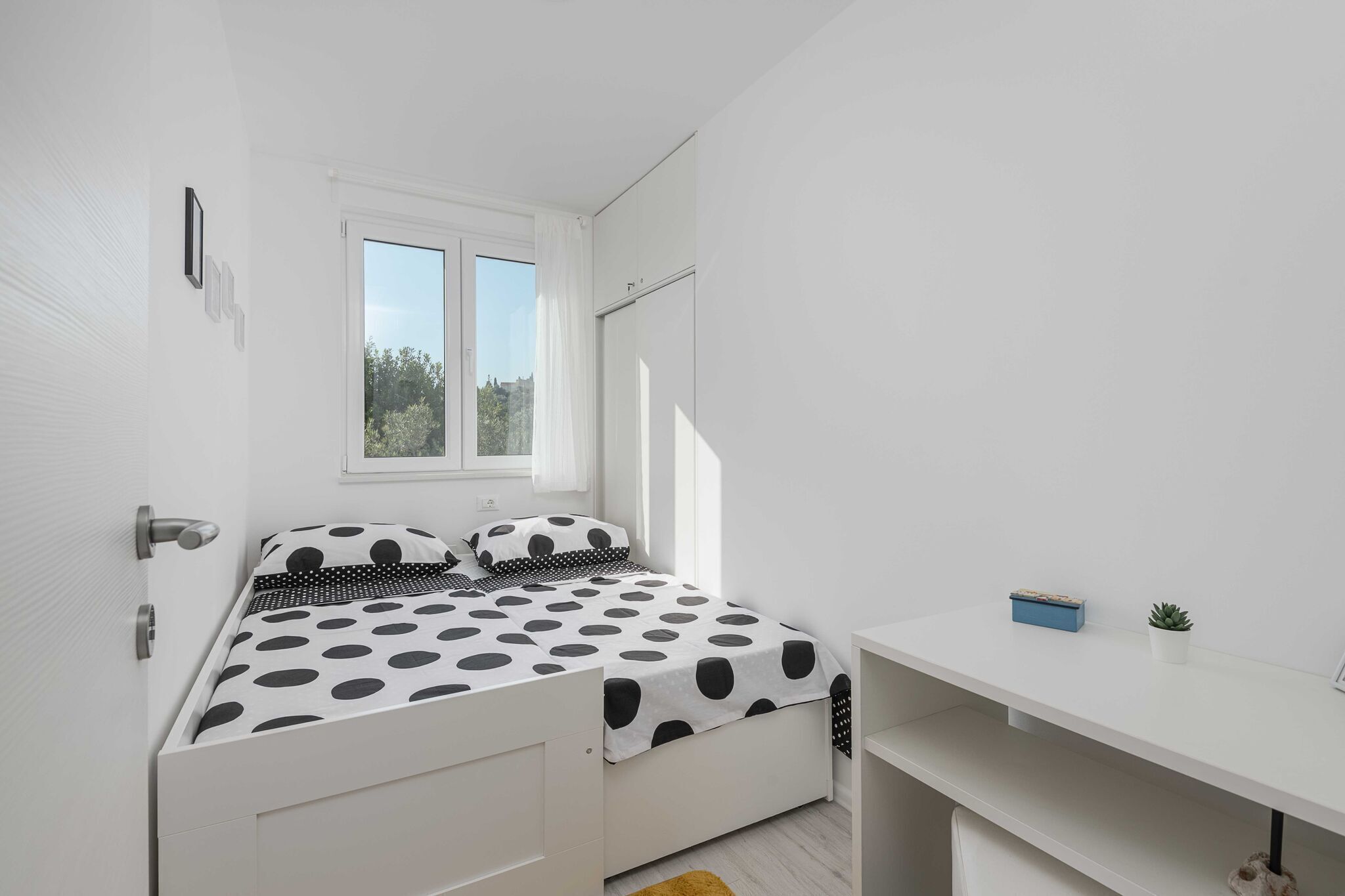 Un dormitorio con una cama, un escritorio, una ventana y una planta pequeña.