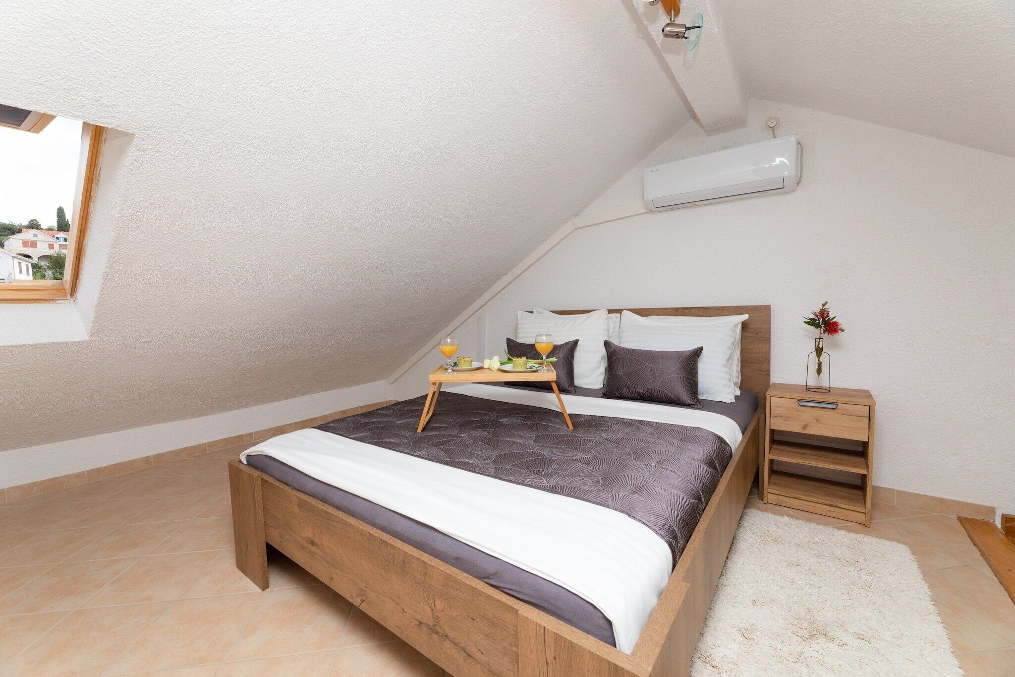 A bedroom with a sloped ceiling, a wooden bed, a bedside table, and a small window.