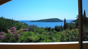 Une vue depuis un balcon abrité, donnant sur un paysage côtier avec un ciel bleu dégagé, une végétation luxuriante et une île lointaine.
