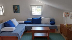 Un salon moderne avec un canapé d’angle, une table basse en bois et un petit meuble. Une fenêtre laisse entrer la lumière naturelle et un tableau orne le mur.