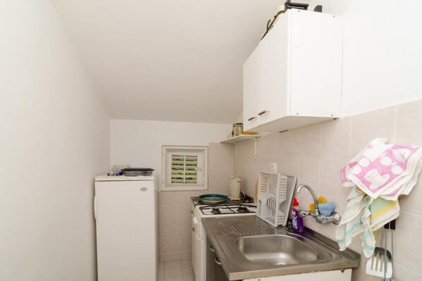 Eine kleine Küche mit Kühlschrank, Herd, Spüle und weißen Schränken.