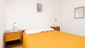 Ein Schlafzimmer mit einem Einzelbett, einem Nachttisch mit Lampe, einem kleinen Tisch mit Kerze und einem Gemälde an der Wand.