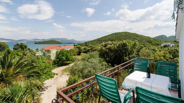 Ein Balkon mit Tisch und Stühlen mit Blick auf einen Strand und eine gebirgige Landschaft.
