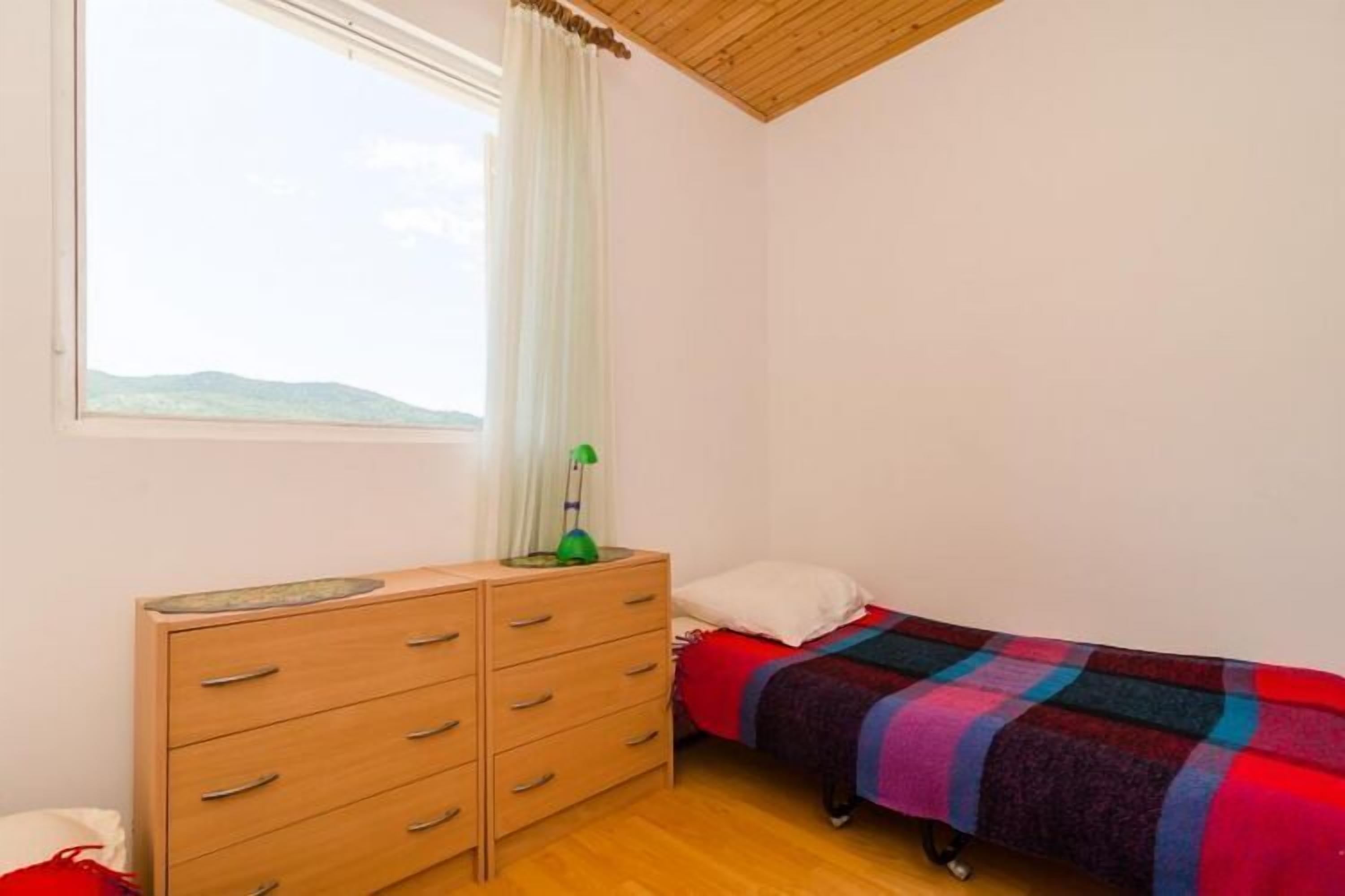 Een slaapkamer met een bed, een dressoir, een raam met uitzicht op het landschap en een lamp op het dressoir.