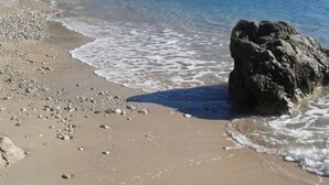 A beach with clear water, pebbles, and a large rock.