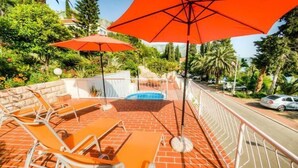 A rooftop pool area with orange lounge chairs and umbrellas, surrounded by a brick wall and greenery. - Guest House Villa Nina- Double Room with Garden View (S3 -Supetar) (Mlini)