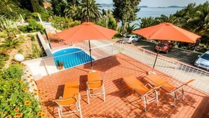 A rooftop pool area with orange chairs and umbrellas, surrounded by greenery and a view of the sea. - Guest House Villa Nina- Double Room with Garden View (S3 -Supetar) (Mlini)