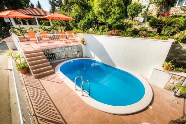 A swimming pool with a stone wall and steps leading up to a patio area with outdoor furniture and umbrellas.