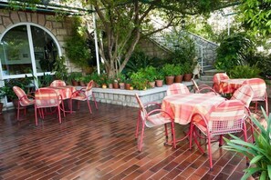 An outdoor patio with red metal chairs and tables, surrounded by potted plants and a stone wall.