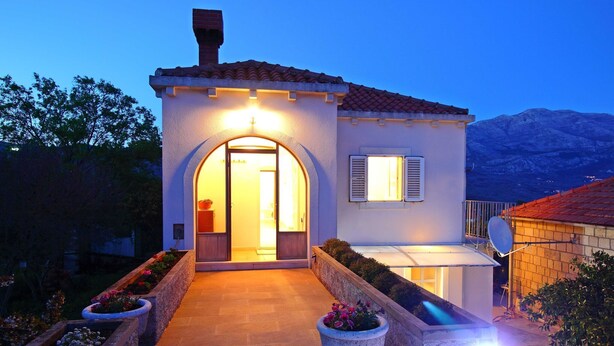 A two-story house with a tiled roof, an arched entrance, and a satellite dish. - Apartment Marita - One Bedroom Apartment with Balcony (Cilipi)