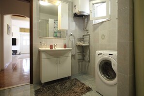 Une salle de bain équipée d’un lavabo, d’un miroir, d’un porte-serviettes, d’une douche et d’un lave-linge.