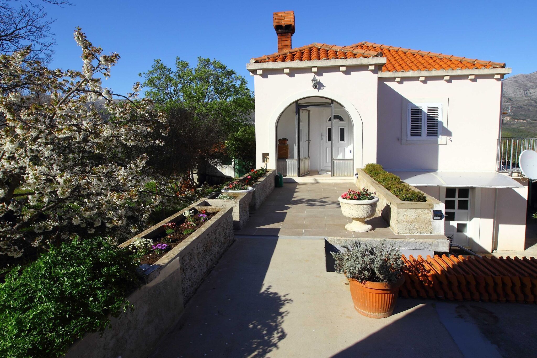 A small, single-story building with a tiled roof, a central archway entrance, and a small balcony with a potted plant.