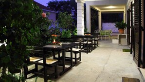 Un patio al aire libre con mesas y sillas, rodeado de plantas y un muro de ladrillo.