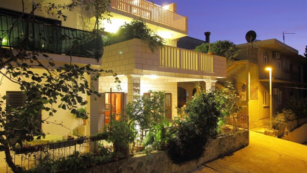Un edificio residencial de varios pisos con balcones, un muro de contención de piedra y plantas en macetas.
