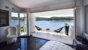 A balcony with a view of a lake and hills, furnished with a white chair, two black chairs, and a potted plant. - Apartment OM - One Bedroom Apartment with Balcony and Sea view (Povlja)
