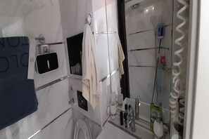 Moderni kylpyhuone, jossa on wc, pesuallas ja peili. Seinällä on pyyhe ja taustalla näkyy suihkutila.