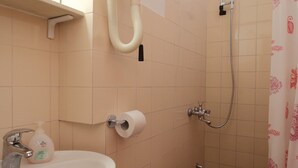Ein Badezimmer mit Waschbecken, Toilettenpapier und einer Dusche mit Brausekopf.