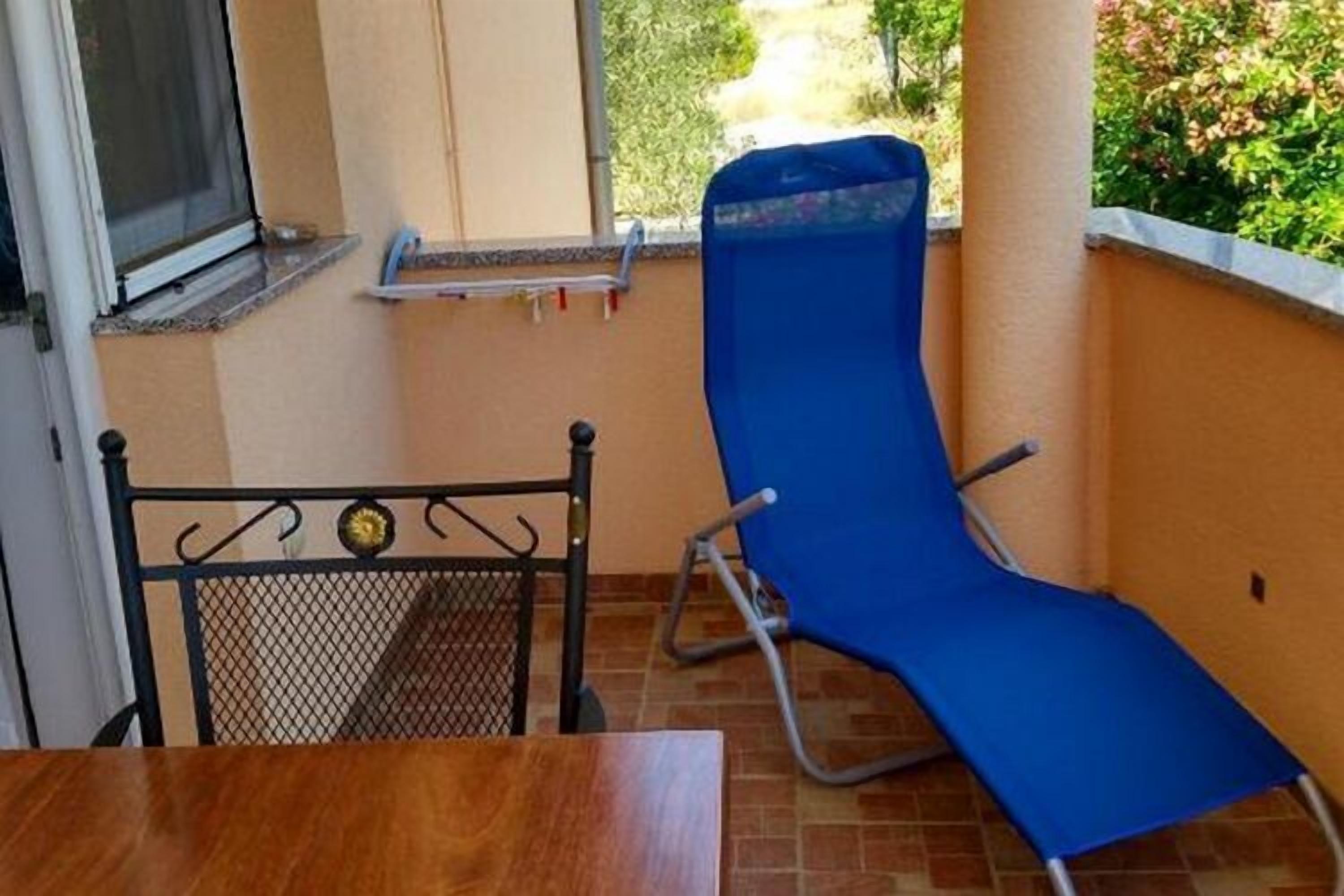 Un balcó amb una cadira blava per relaxar-se, una taula petita i una cadira de metall.