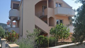 Ein mehrgeschossiges Wohngebäude mit Balkonen, einer flachen Dachterrasse und einem Gartenbereich mit verschiedenen Pflanzen.