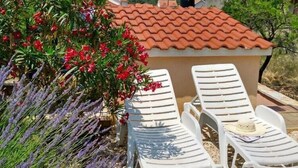 Eine Terrasse mit weißen Kunststoffliegen, ein kleines Gebäude mit Ziegeldach und umgebenden Lavendelpflanzen.