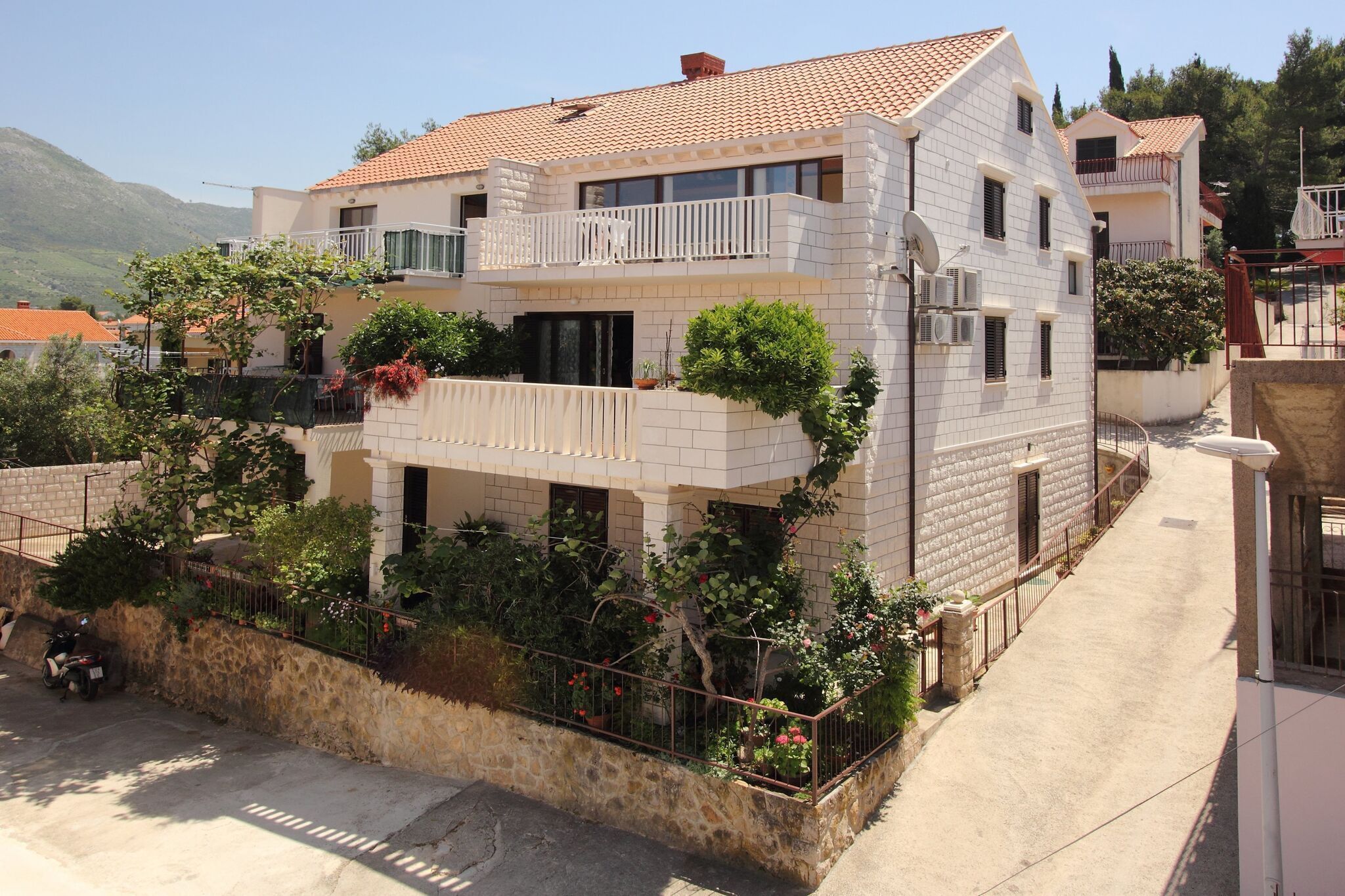 Un edificio residenziale a due piani con un balcone, un muro in pietra e un vialetto lastricato.