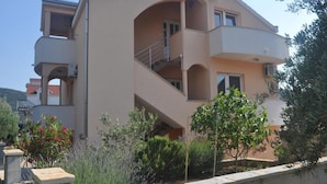 Un immeuble résidentiel à plusieurs étages, doté de balcons, d’un toit plat et d’un espace jardin agrémenté de diverses plantes.