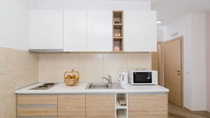 Una cocina compacta con armarios blancos, microondas, lavaplatos y una cesta de frutas.