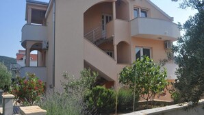 Ein mehrgeschossiges Wohngebäude mit Balkonen, einer flachen Dachterrasse und einem Gartenbereich mit verschiedenen Pflanzen.