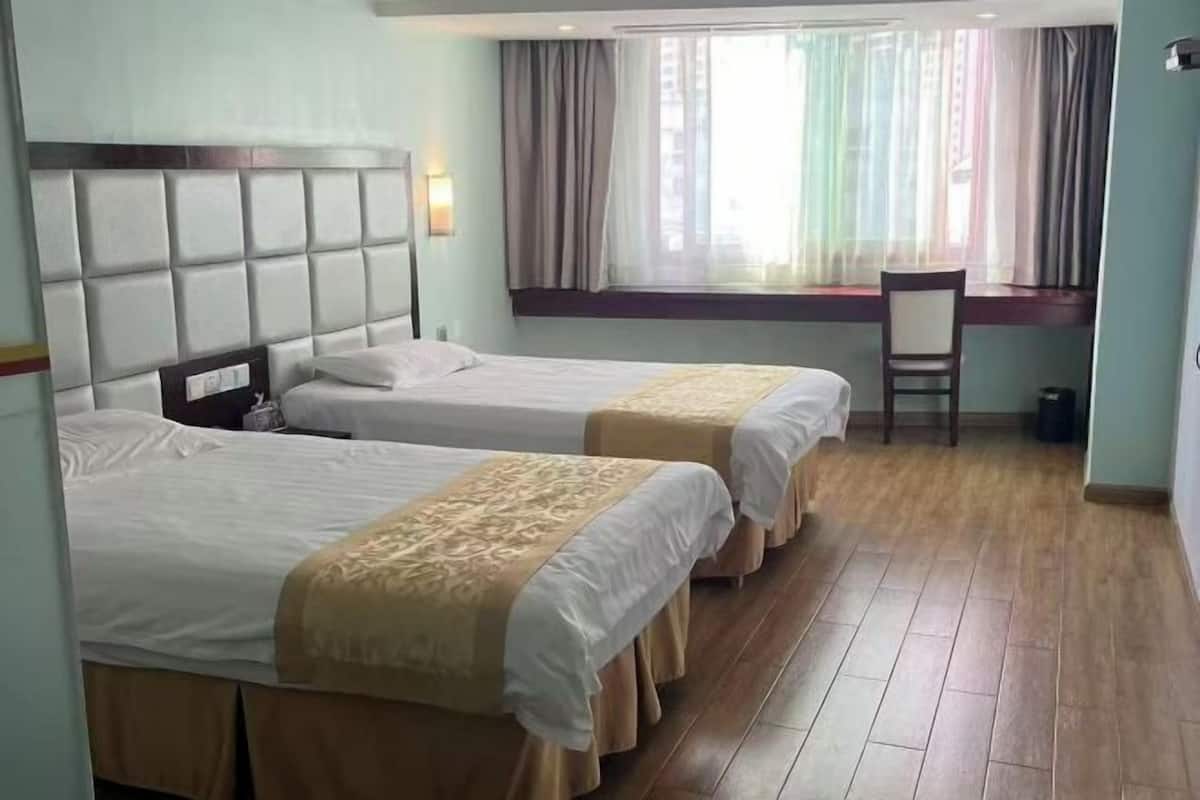 A hotel room with two beds, a desk, and a window with curtains.